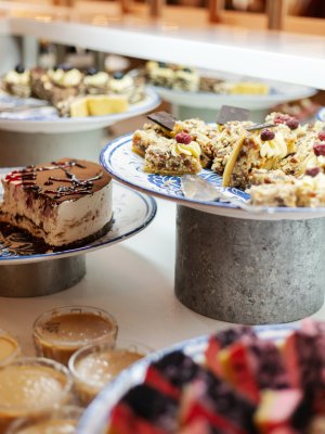 A stunning variety of desserts is showcased at a lively event, featuring cakes, bars, and colorful treats arranged on decorative plates. Sweet aromas fill the air.