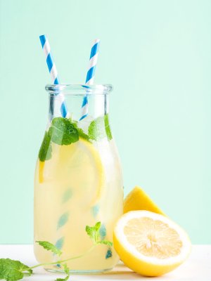 Bottle of homemade lemonade with ice and lemons, paper straws and pastel mint  background, selective focus