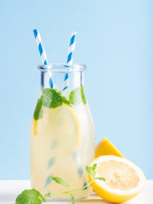 Bottle of homemade lemonade with mint, ice and lemons, paper straws and pastel blue background, selective focus