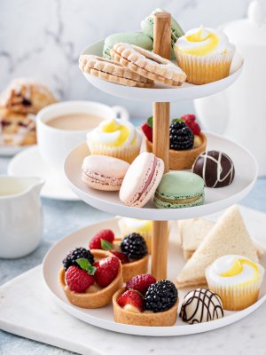 Spring or summer dessert table, three tiered tray with variety of desserts and sandwiches for tea